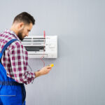 A man in a checkered shirt checks the operation of an air conditioner repair.