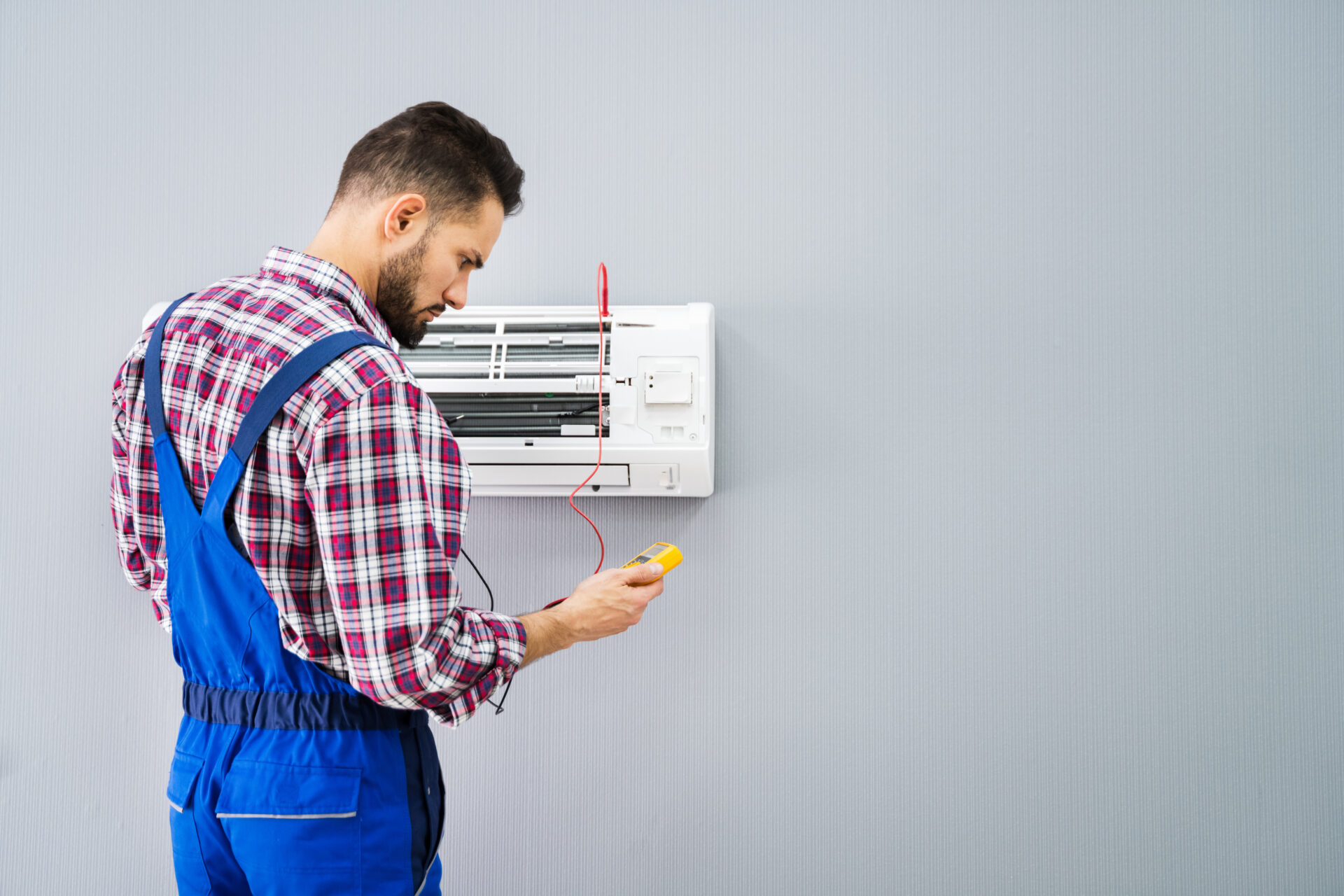 A man in a checkered shirt checks the operation of an air conditioner repair.