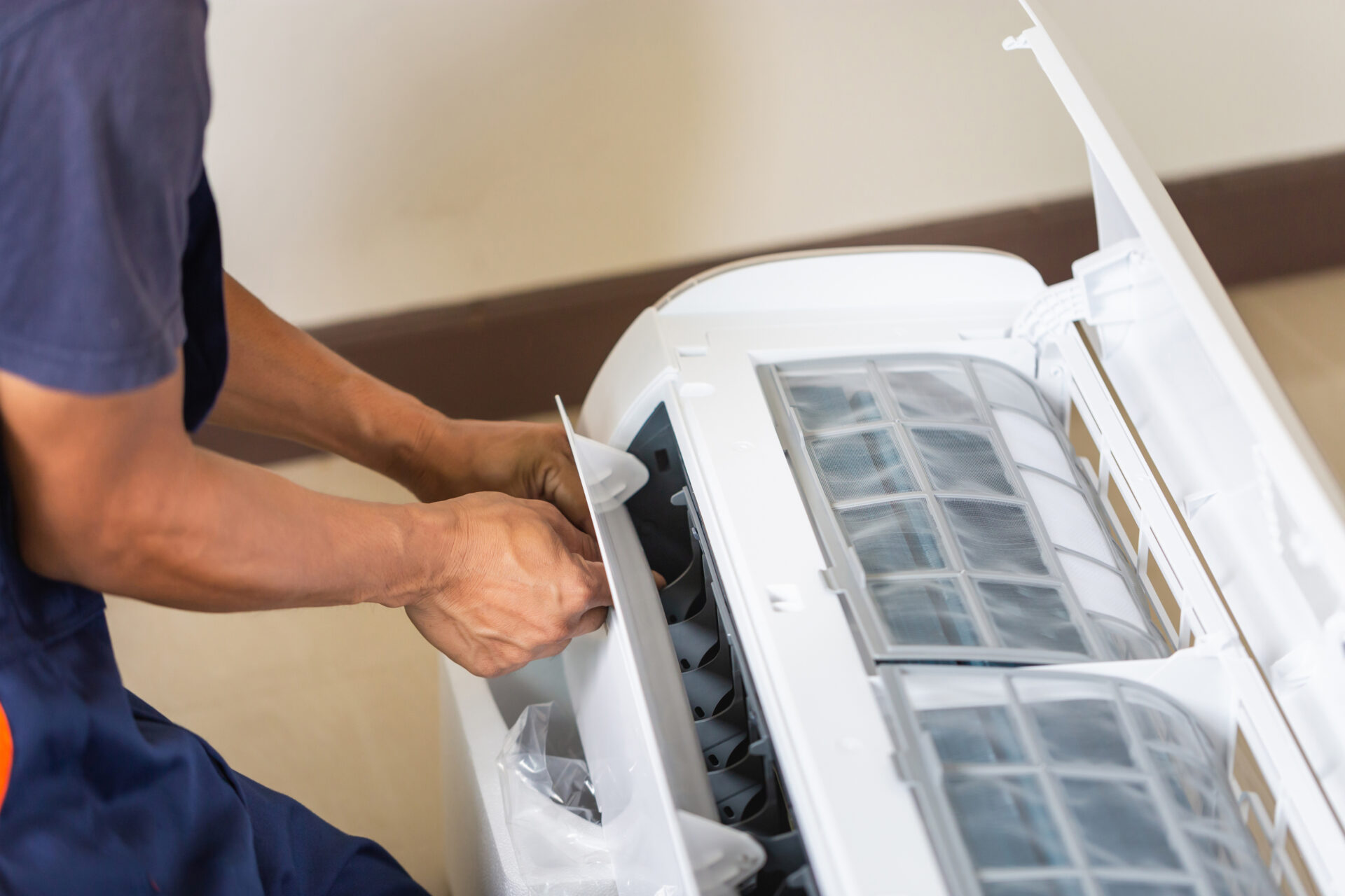 A male worker in a blue T-shirt is doing air conditioner repair