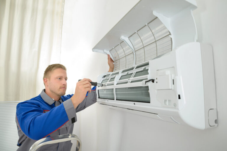 Blonde ac installation technician in blue gray uniform installing air conditioner in room
