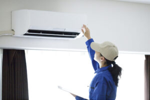 Female with dark hair in a ponytail wearing a blue uniform and beige cap is doing hvac repair