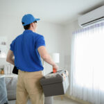Worker in a uniform and a blue cap with a suitcase of tools is about to do an hvac repair