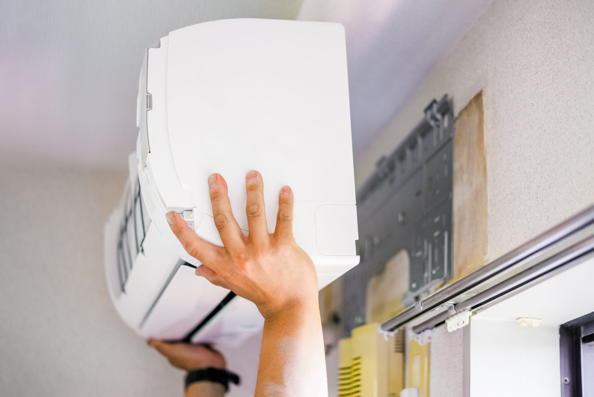 Male hands with a black watch on the left hand holding a white air conditioner and doing hvac installation